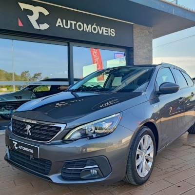 Carro Peugeot cinzento metálico estacionado em frente a loja RC Automóveis