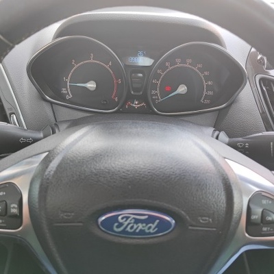 Volante de carro Ford preto em couro com painel de instrumentos atrás mostrando velocímetro e conta-rotações