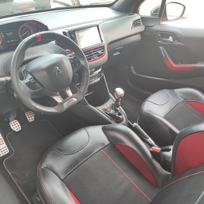 Interior de carro Peugeot com volante em couro preto e detalhes vermelhos.