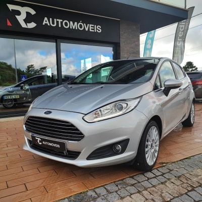 Ford Fiesta prateado estacionado em frente a loja RC AUTOMÓVEIS