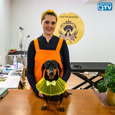Mulher com avental laranja segura cão preto com gola amarela plissada numa mesa marrom