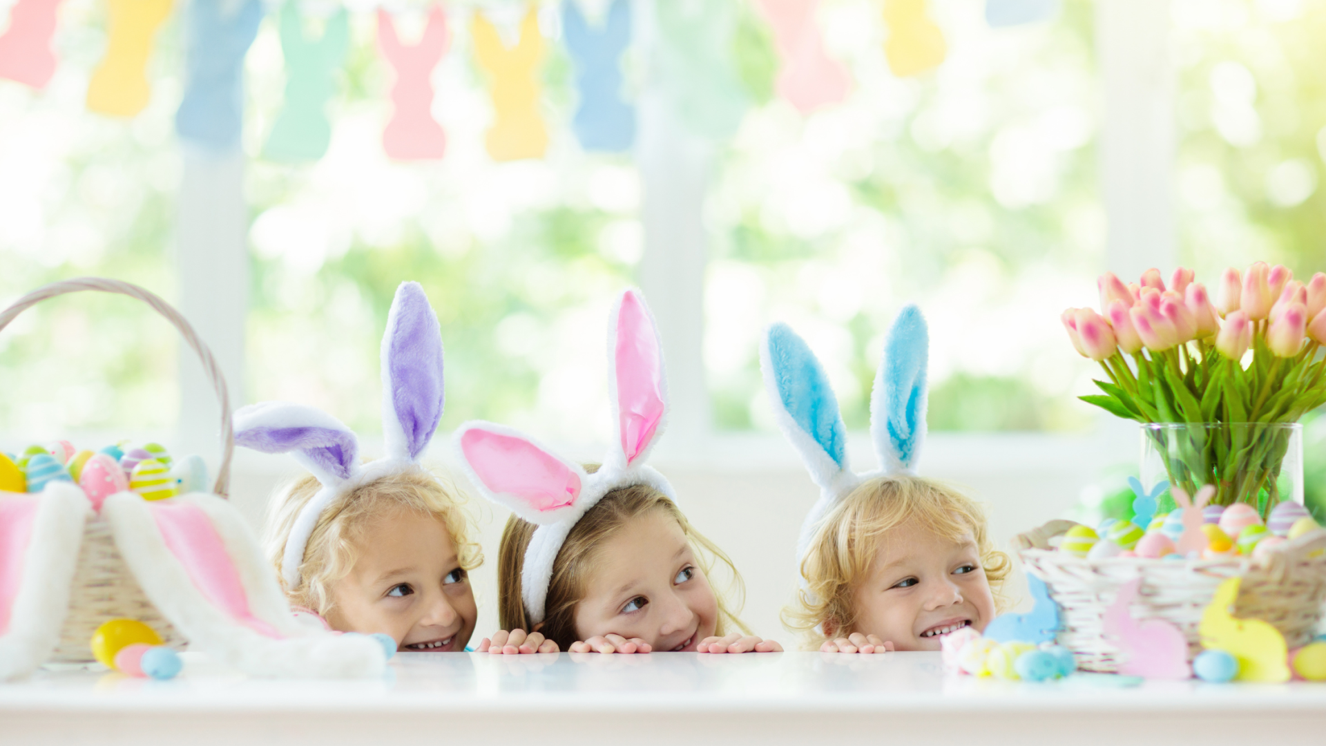 Crianças com tiaras de orelhas de coelho e decoração de Páscoa na mesa