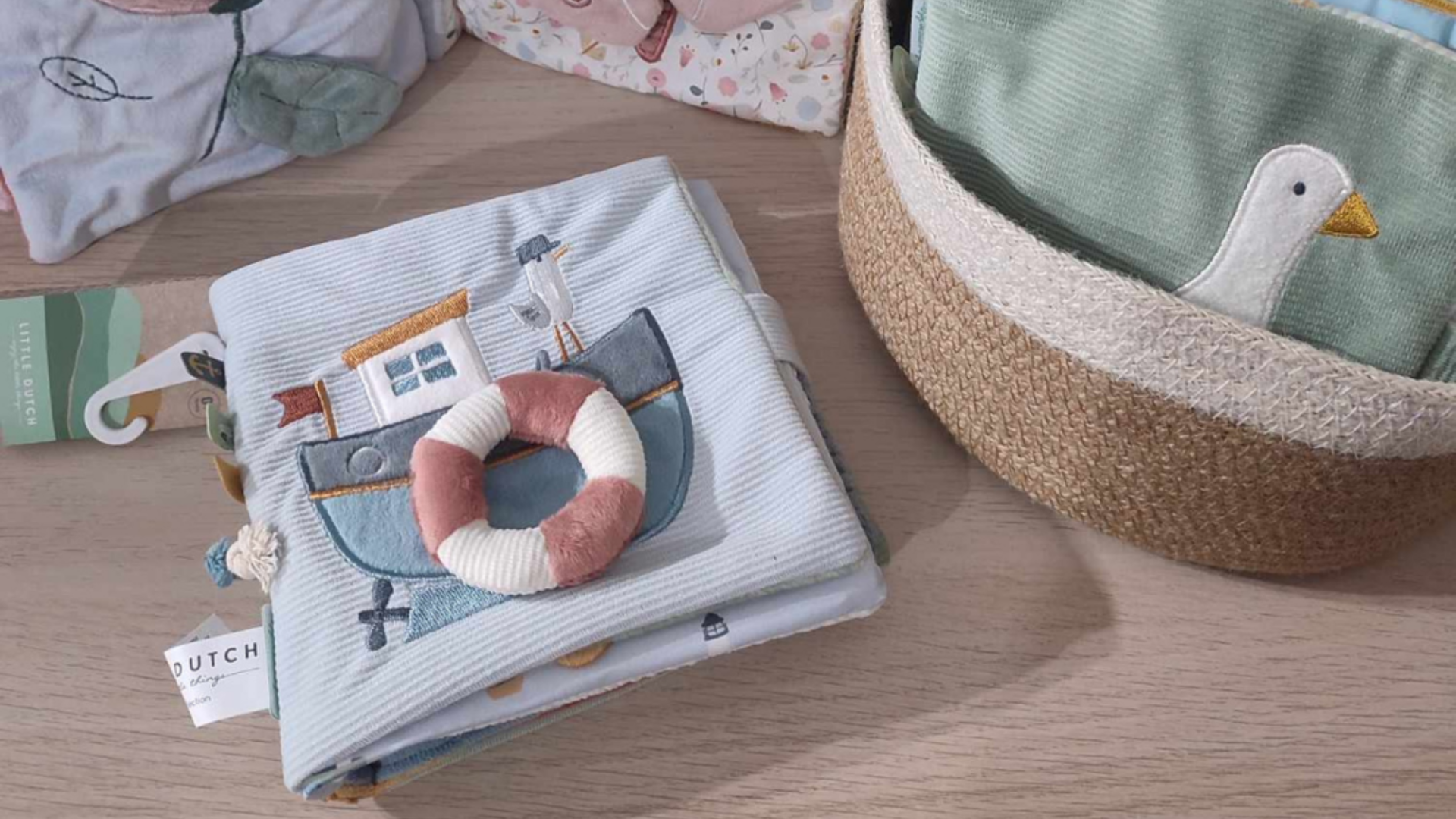 Sugestões de Livros para Bebés Livro de tecido com ilustração de barco e cesto de verga com tecido e bordado de pato