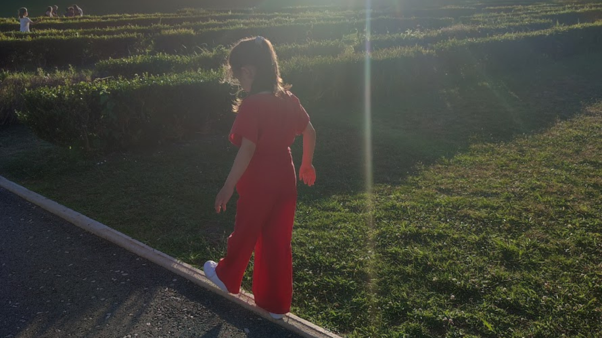 Mulher de costas em macacão vermelho em jardim ao pôr do sol