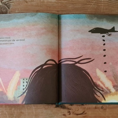 Livro ilustrado aberto mostrando texto em português e ilustração com aviões e cabelos castanhos.