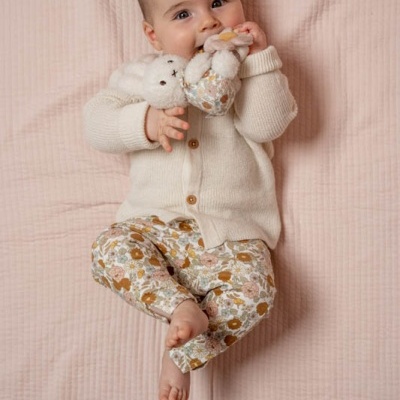Bebé com camisola creme e calças florais a segurar brinquedo de peluche deitado em colchão rosa