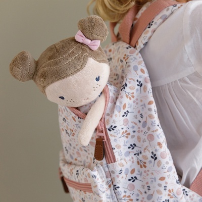 Criança com mochila floral rosa e boneca de pano castanha com laço cor-de-rosa