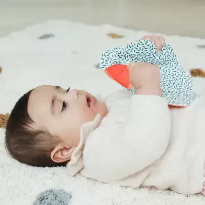 Bebé deitado a segurar acessório de tecido com padrão abstrato