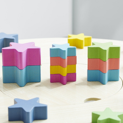 Peças de madeira em formato de estrelas coloridas empilhadas sobre mesa de madeira clara