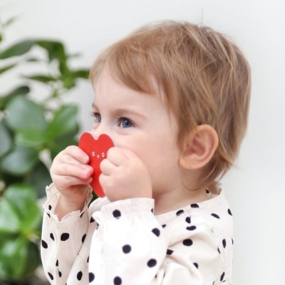 Criança com brinquedo vermelho em forma de flor e camisa branca com bolas pretas