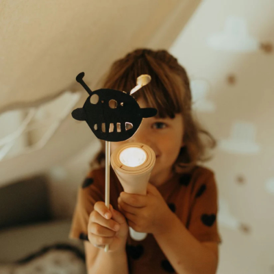Criança segurando lanterna branca e figura decorativa preta em quarto claro