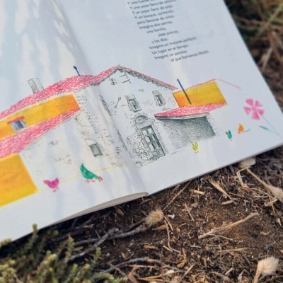 Livro aberto com ilustração de casa colorida sobre terra com vegetação seca