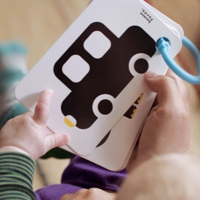 Livro infantil de cartão com imagem de carrinho preto e branco, segurado por mãos de adulto e bebé.