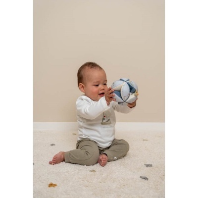 Bebé sentado a brincar com bola de tecido azul e branca num tapete creme.