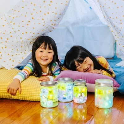 Duas crianças numa tenda branca com estrelas douradas e frascos iluminados