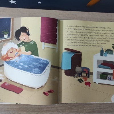 Livro infantil aberto com ilustração de criança na banheira e texto em português