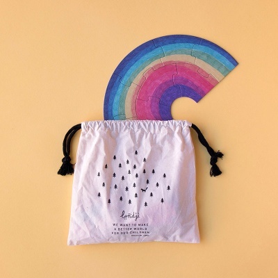 Saco branco com cordões pretos e texto impresso ao lado de arco-íris de madeira colorido