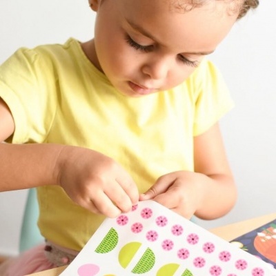 Criança com t-shirt amarela a colar autocolantes coloridos num livro