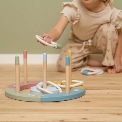 Brinquedo educativo redondo em madeira com postes coloridos e anéis brancos no chão de madeira