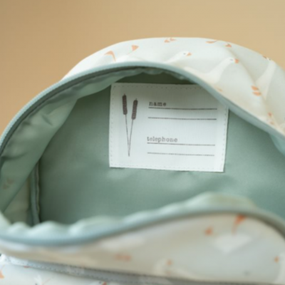 Interior de mochila branca com padrão alaranjado e etiqueta para nome e telefone