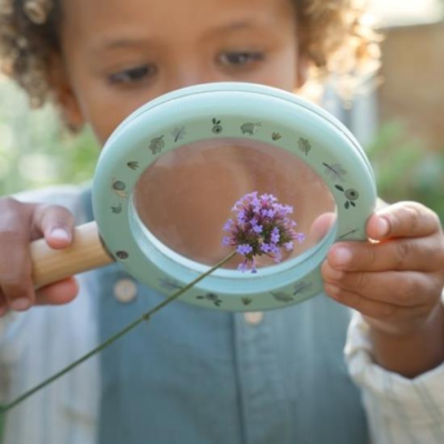 Lupa verde com pega de madeira a ser usada por menina para observar flor roxa