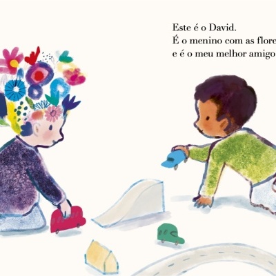 Duas crianças a brincar com carros de brinquedo e trilho, uma com flores no cabelo, a outra de verde, texto em português ao lado