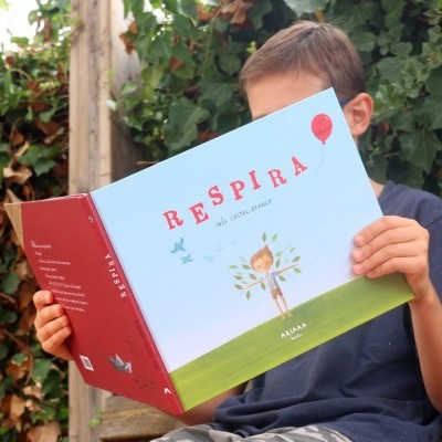 Criança a ler livro 'RESPIRA' sentada num banco de madeira num jardim