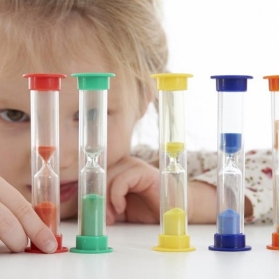 Cinco ampulhetas coloridas numa mesa com criança ao fundo