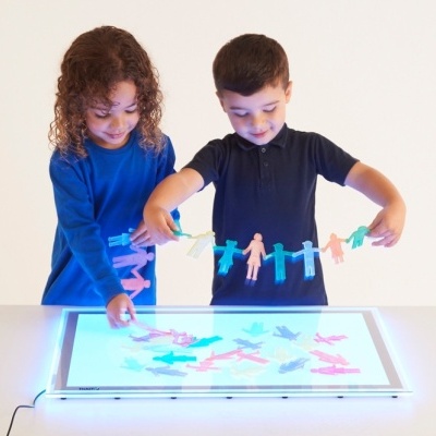 crianças a brincar com figuras humanas coloridas sobre mesa iluminada