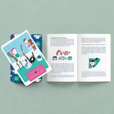 Livro aberto com texto em português e ilustrações de mulheres, caixa colorida com padrão floral e cartões sobre a caixa