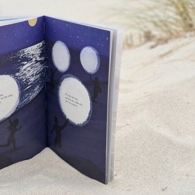 Livro ilustrado aberto no areia branca com ilustrações e texto em inglês