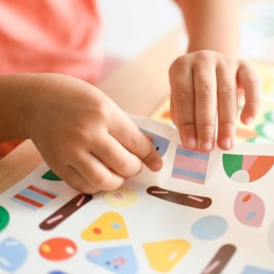 Mãos de criança a aplicar autocolantes coloridos em papel branco.