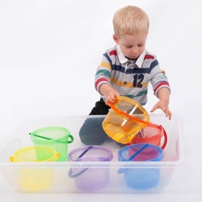 Menino a brincar com copos plásticos coloridos num recipiente transparente