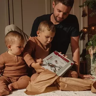 Duas crianças e um homem com uma caixa de brinquedo junto a uma árvore de Natal