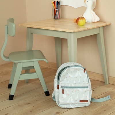 Mesa e cadeira verdes com tampo de madeira clara, mochila azul clara com padrão de gansos no chão, maçã e lápis em copo na mesa
