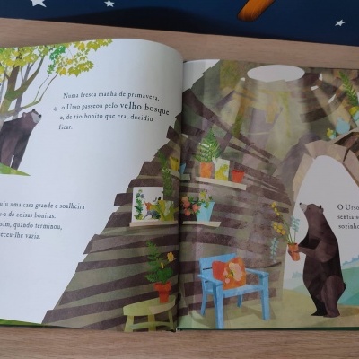 Livro infantil aberto com ilustrações de um urso e uma casa dentro de uma árvore