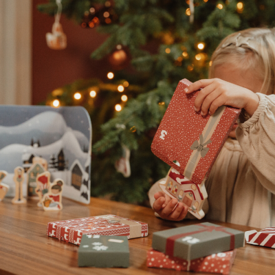 Caixa de presente vermelha com padrão de estrelas e laço, sobre mesa com outras caixas e árvore de Natal ao fundo