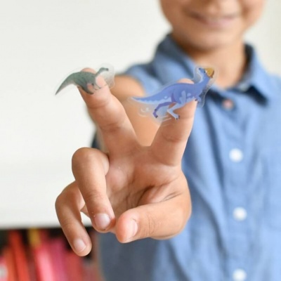 Dois brinquedos de dinossauros nas pontas dos dedos de uma criança com camisa azul.