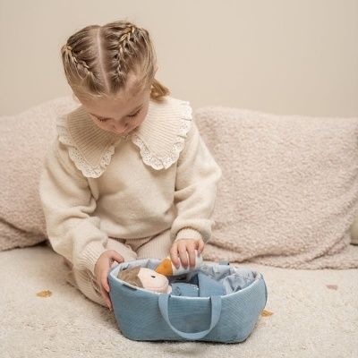 Criança com camisola bege de malha e gola rendada a brincar com mala de tecido azul e boneca