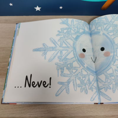 Livro infantil aberto com ilustração de floco de neve sorridente e texto 
