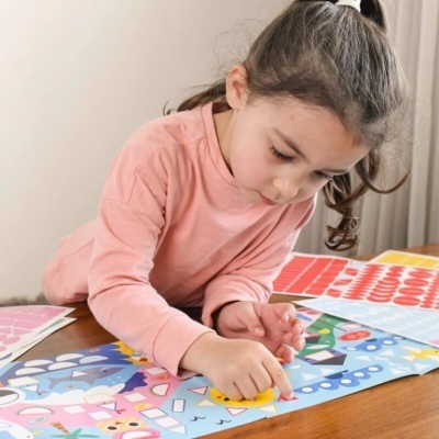 Criança a colar autocolantes num tabuleiro de jogo colorido numa mesa de madeira