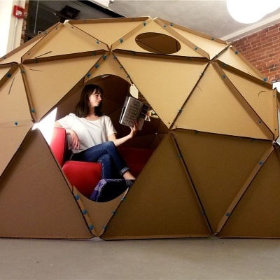 Estrutura geodésica castanha com painéis triangulares e pessoa a ler no interior