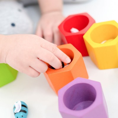 Peças de madeira coloridas em forma de hexágonos e mão de criança interagindo
