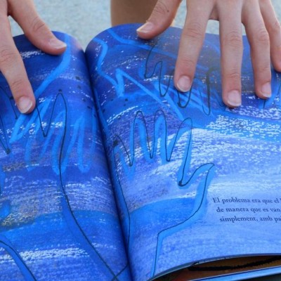 Livro aberto com ilustrações azuis e texto em português sobre mãos desenhadas