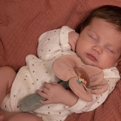 Bebé adormecido com roupa branca às bolinhas e peluche em forma de flor