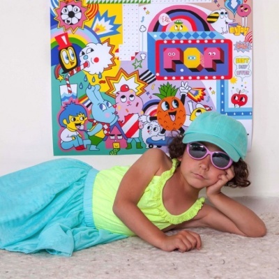 Menina de óculos de sol rosa e vestido colorido junto a parede com desenhos animados