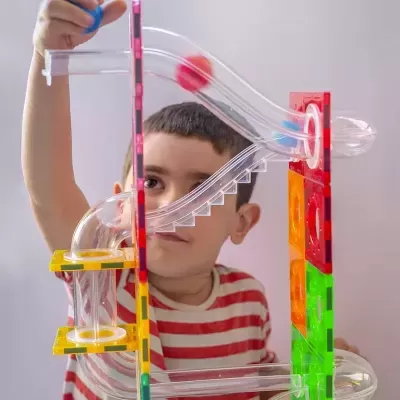 Criança a brincar com brinquedo de tubos transparentes e painéis coloridos.