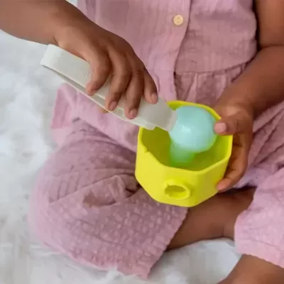 Criança usando roupa cor-de-rosa com dispenser branco e recipiente amarelo com líquido azul