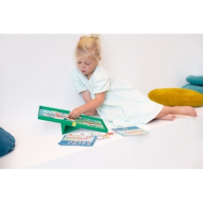 Menina loira brincando com jogo educativo em superfície branca com almofadas coloridas