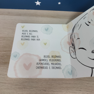Livro infantil aberto com texto em português e ilustração de criança sorridente com olhos fechados e manchas coloridas